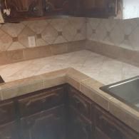 Corner kitchen countertop with beige tile backsplash, dark cabinets, and a stainless steel sink