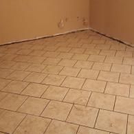 Empty tiled room with beige walls and light floor tiles, viewed from a corner.