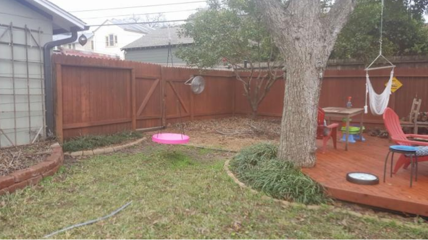 Backyard with wooden fence, tree, patio deck, children’s toys, and a pink pool on the grass