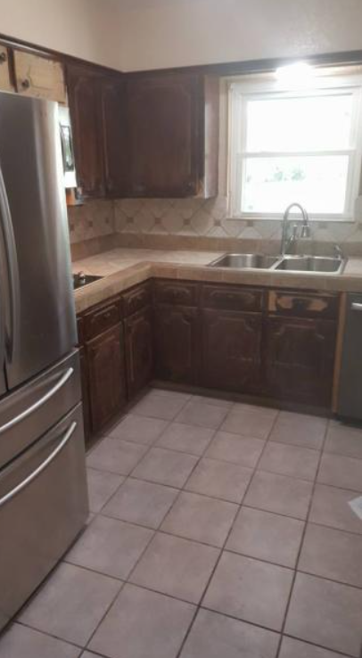 Small kitchen with dark wood cabinets, stainless refrigerator, tile floor, and a window over the sink.