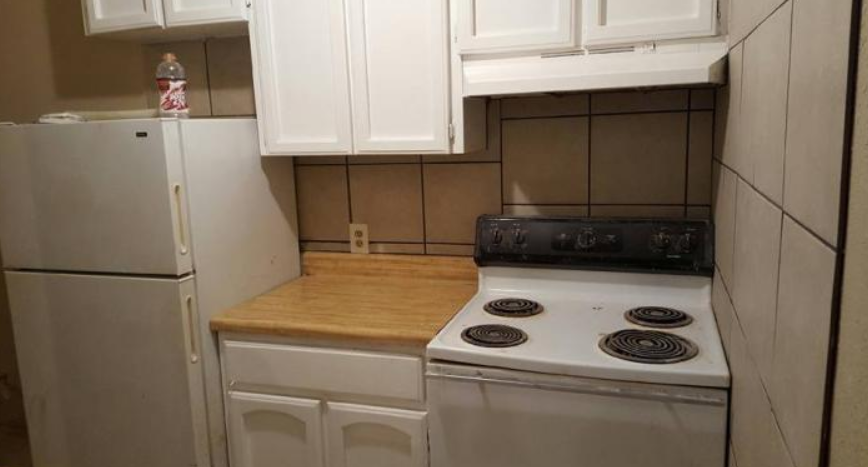 Small kitchen with white cabinets, wood countertop, beige tile walls, and a white stove and refrigerator.