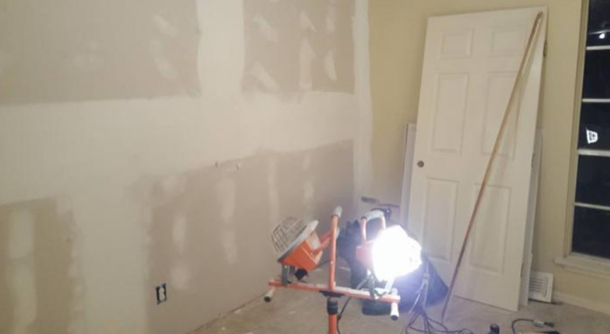 Partially painted room with drywall patches, a door, and a bright work light on a stand