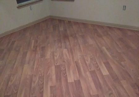 Empty room with wood-look flooring and beige walls, viewed from a corner.