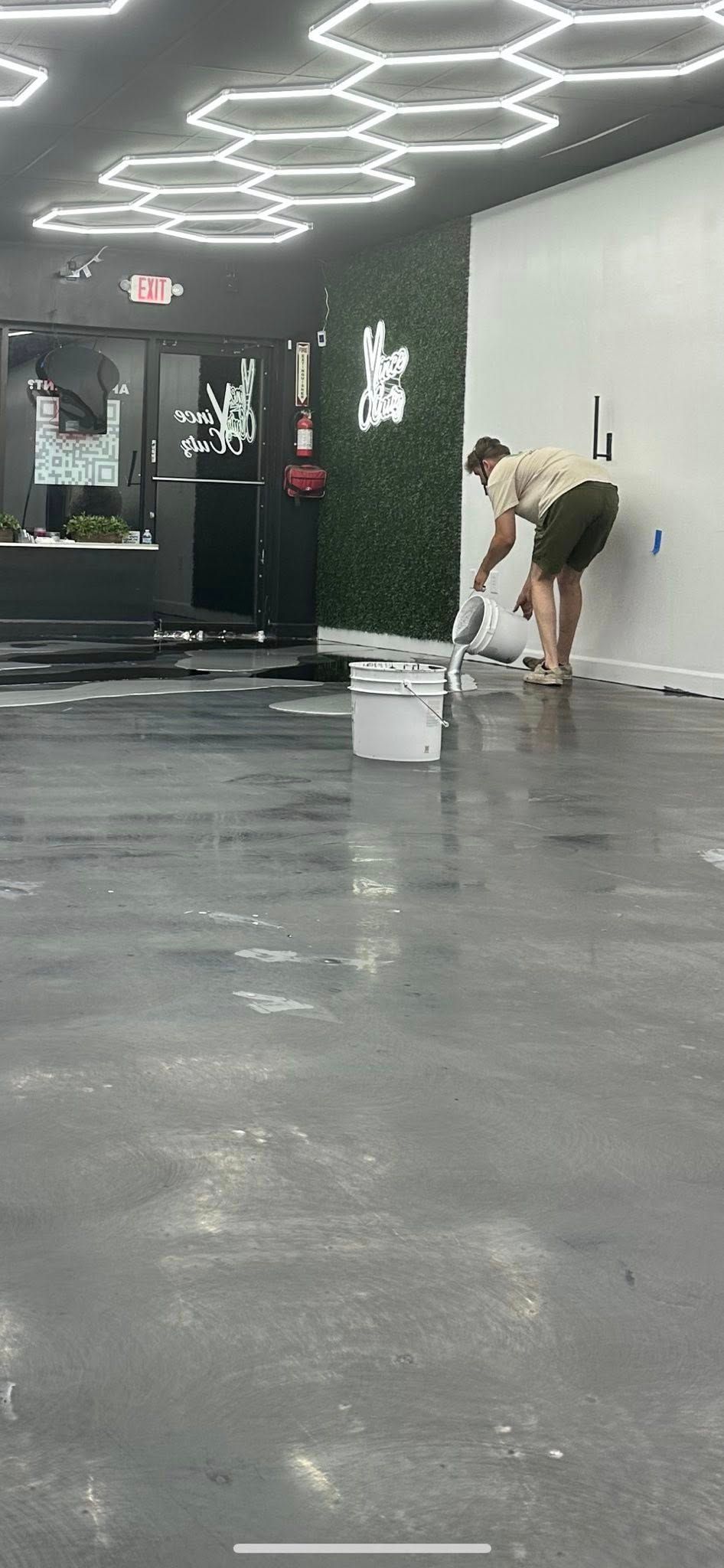 Person mopping a glossy floor in a dark modern hallway with bright ceiling lights.
