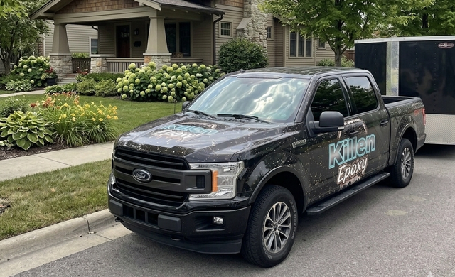 Black pickup truck parked on a residential street in front of a house and garden.