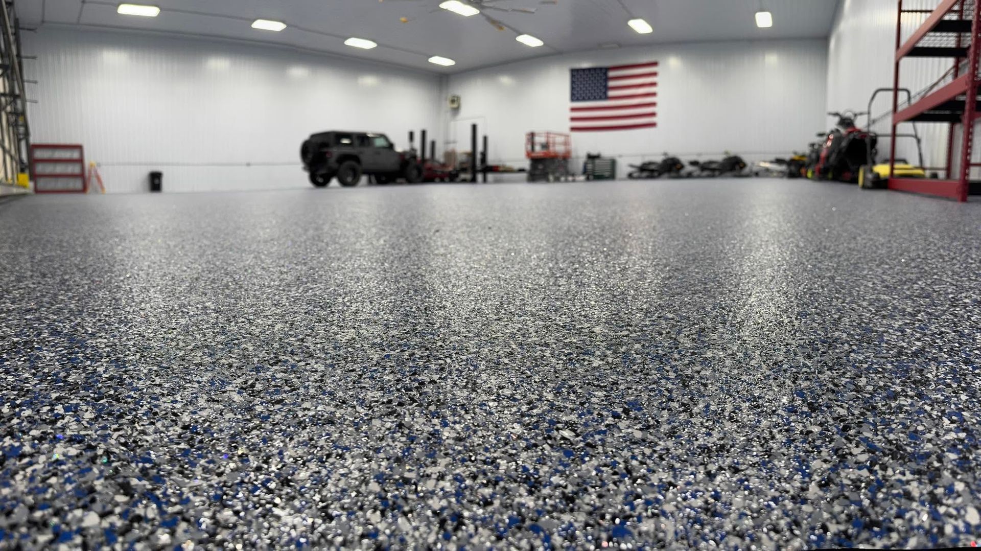 Spacious garage with speckled epoxy floor, cars, tools, and an American flag on the back wall.