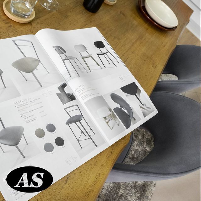 Catalogo aperto di sedie su un tavolo di legno, con sedie e servizi da tavola visibili.