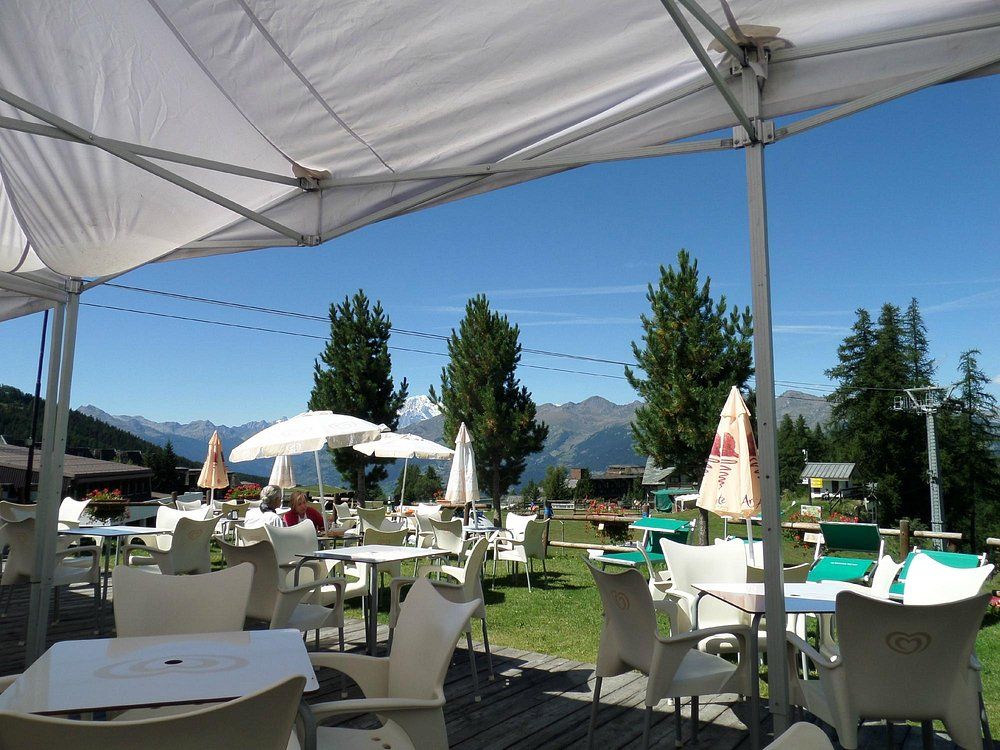 Tavoli e sedie sotto un ombrellone con montagne sullo sfondo
