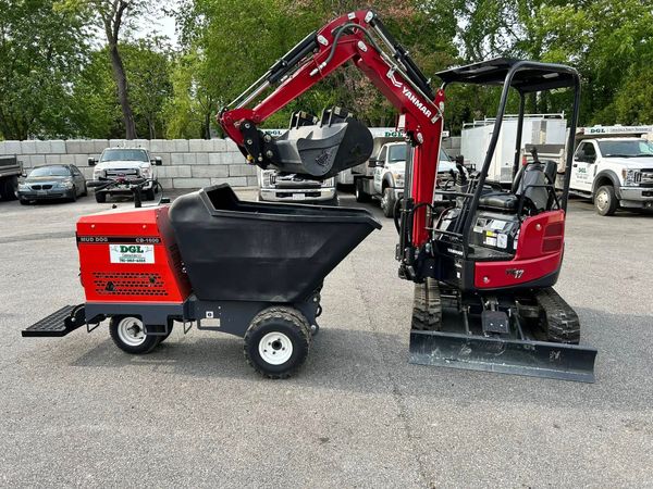 Red skid-steer loader with attached wood chipper and dump hopper on a gravel lot