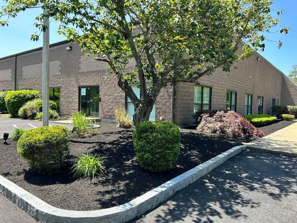 Brick office building with dark mulch landscaping, shrubs, and a tree in front on a sunny day
