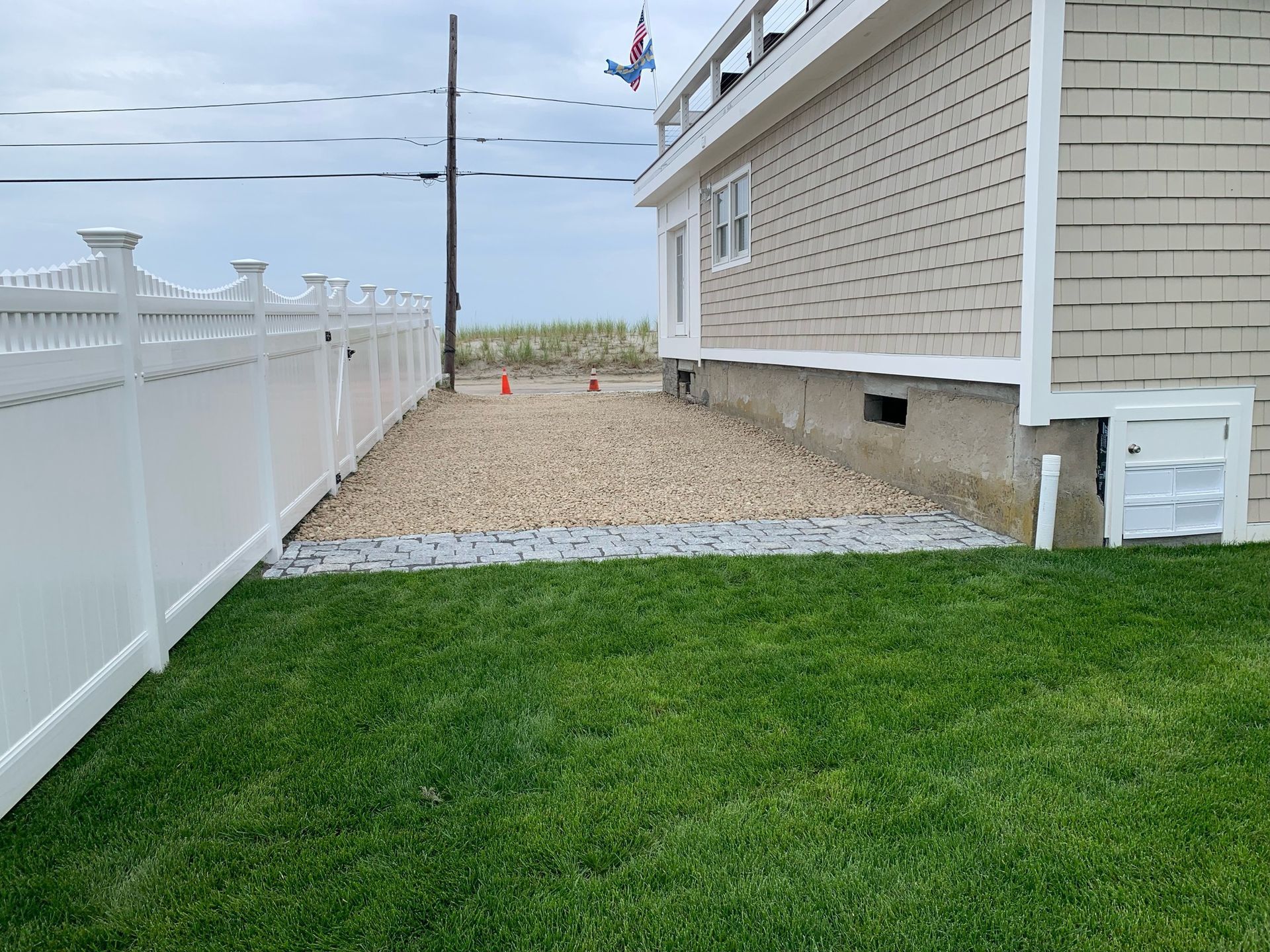 Backyard with green lawn, gravel strip, white fence, and beige house siding