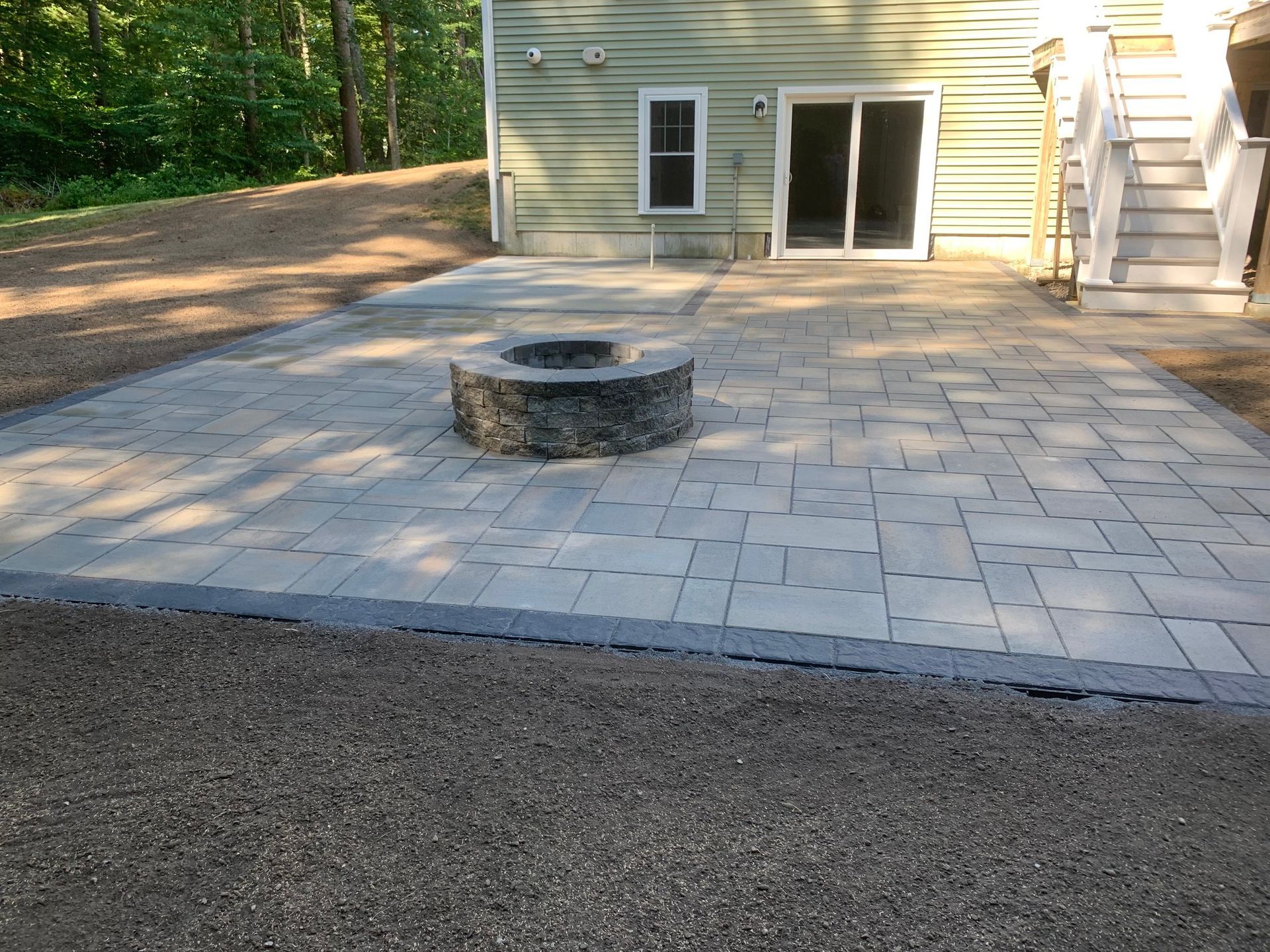 Stone patio with a circular fire pit beside a house and sliding glass doors