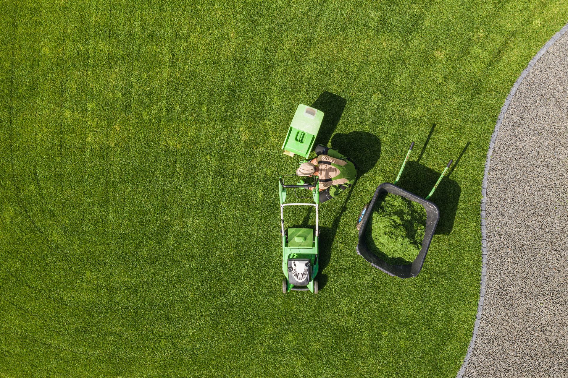 Overhead view of a child riding a green toy tractor on grass beside a black tire swing and gravel path