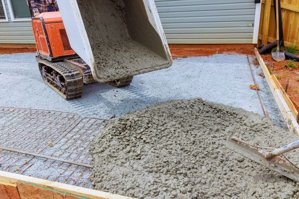 Small construction vehicle unloading wet concrete onto a driveway foundation area.