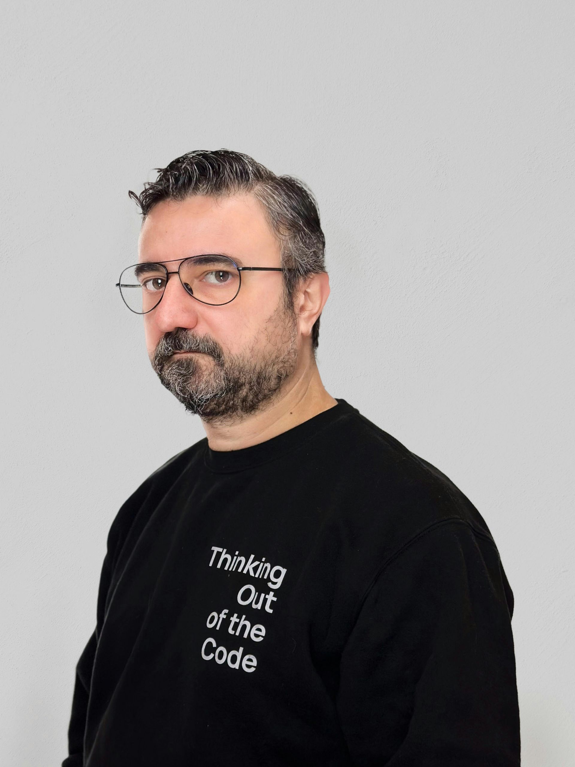 Man in glasses and black shirt with “Thinking out of the Code” text, posed against a light gray background