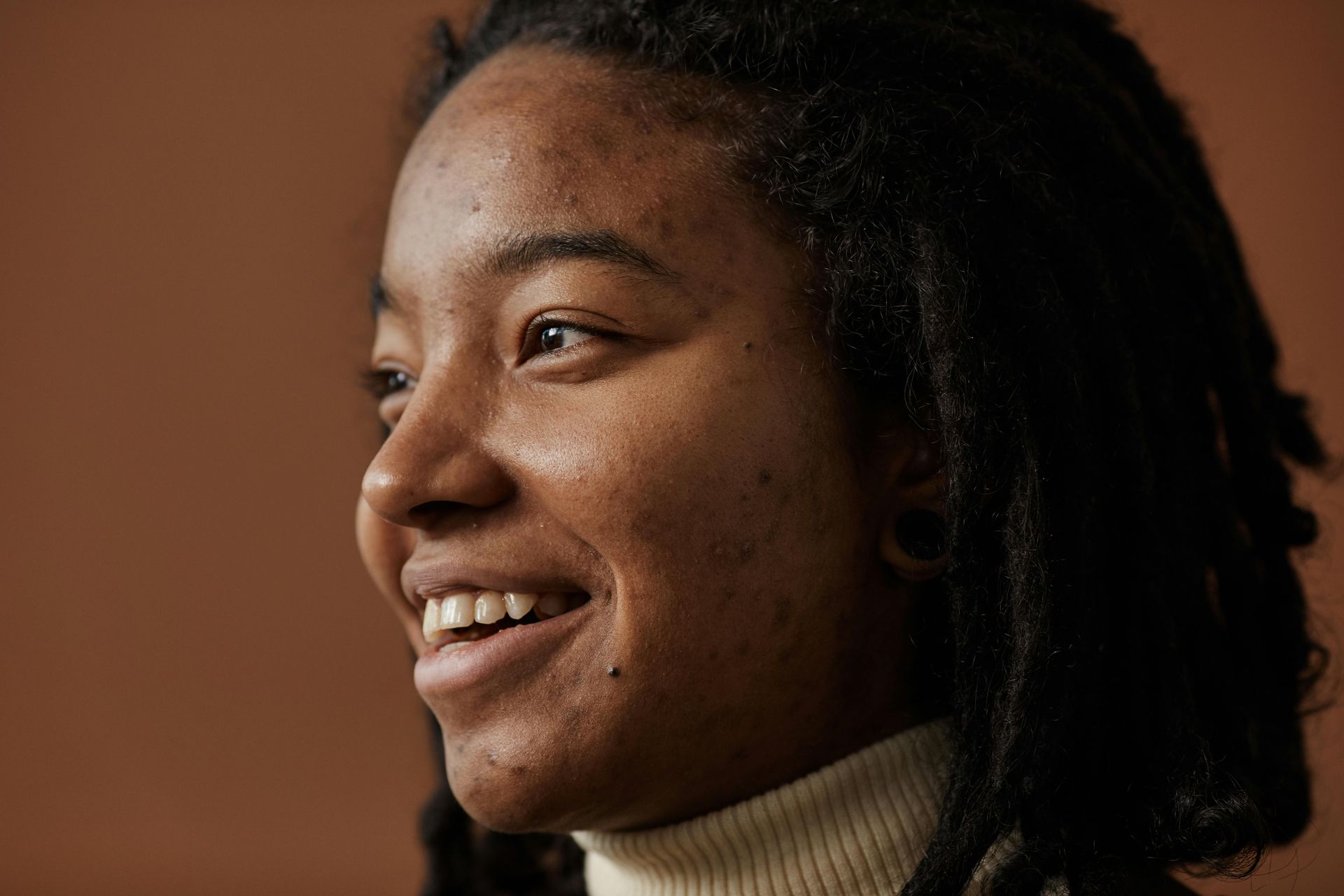 Smiling person in profile against a warm brown background