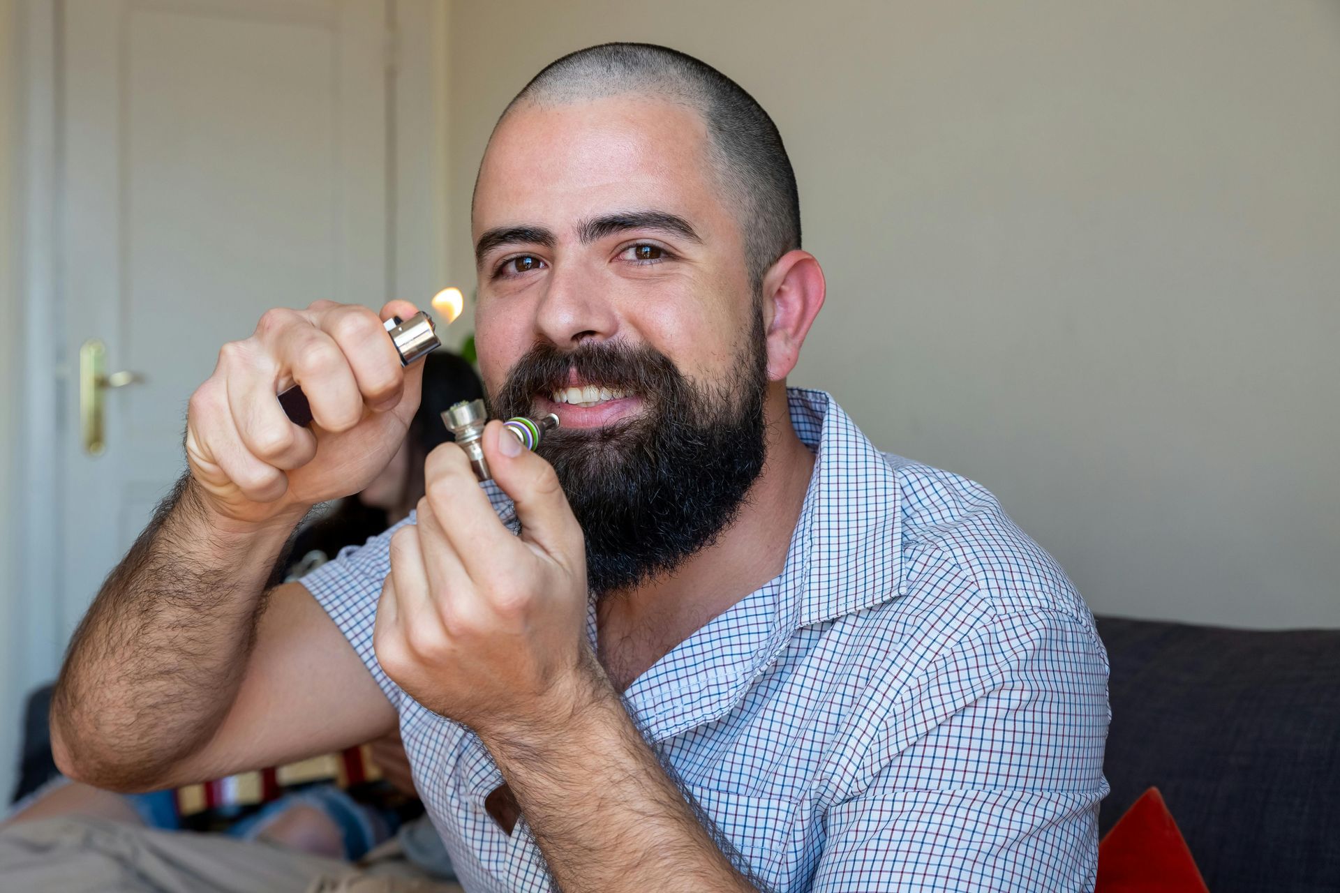 Man smiling while holding a small object near his face in a bedroom, with a white door in the background