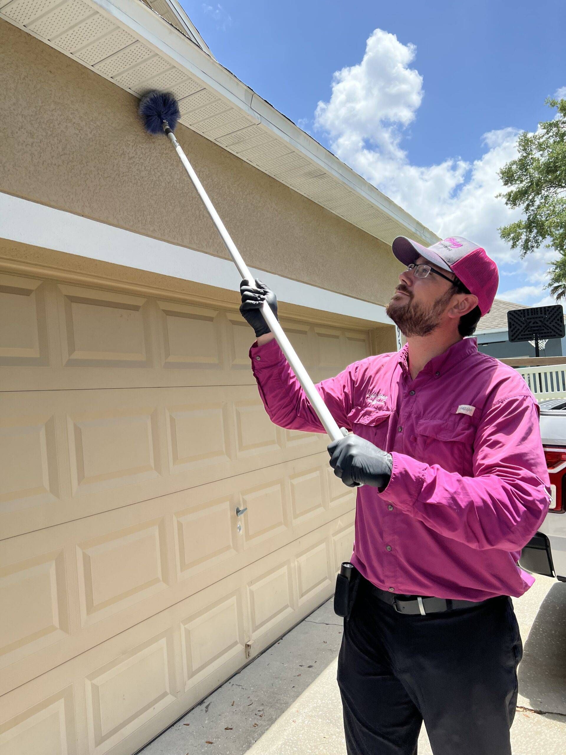 Person using a long pole duster to clean a garage roof edge on a sunny day
