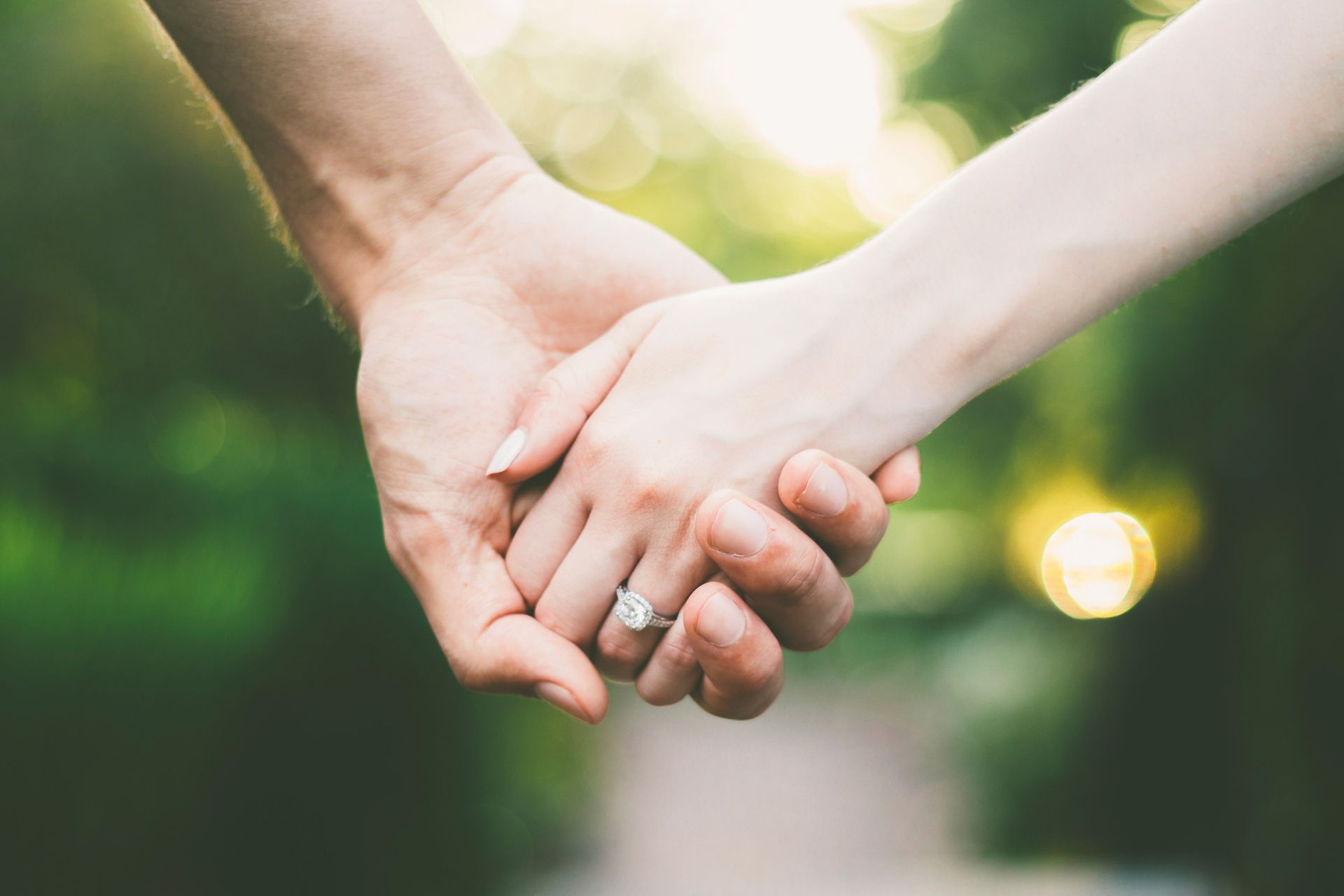 A woman with an engagement ring is holding a man's hand.