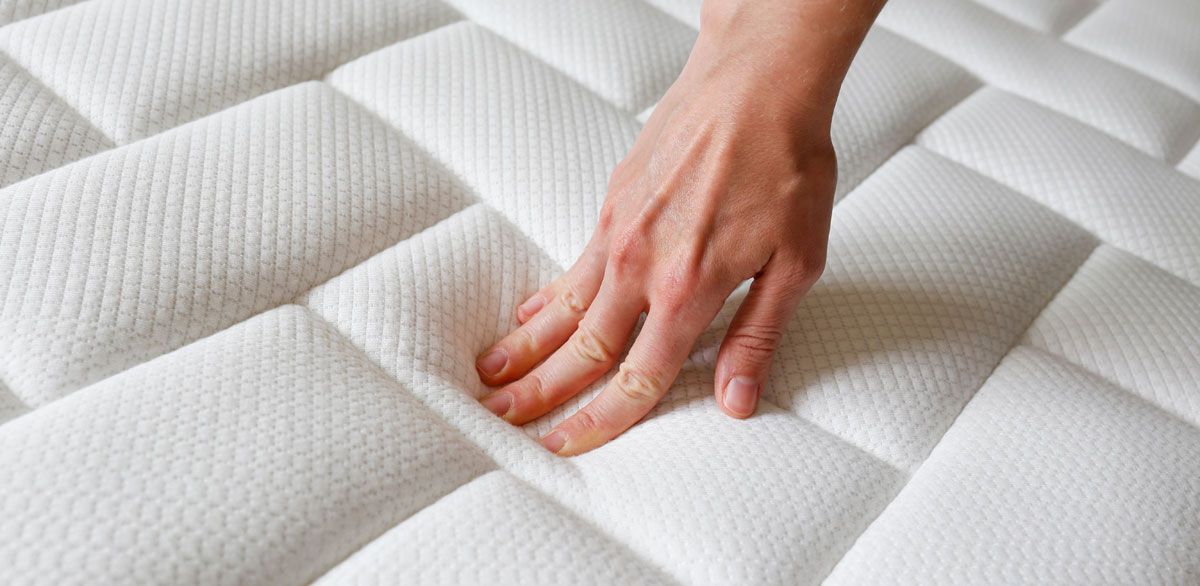 Hand pressing down on a white, quilted mattress, showing its soft texture.
