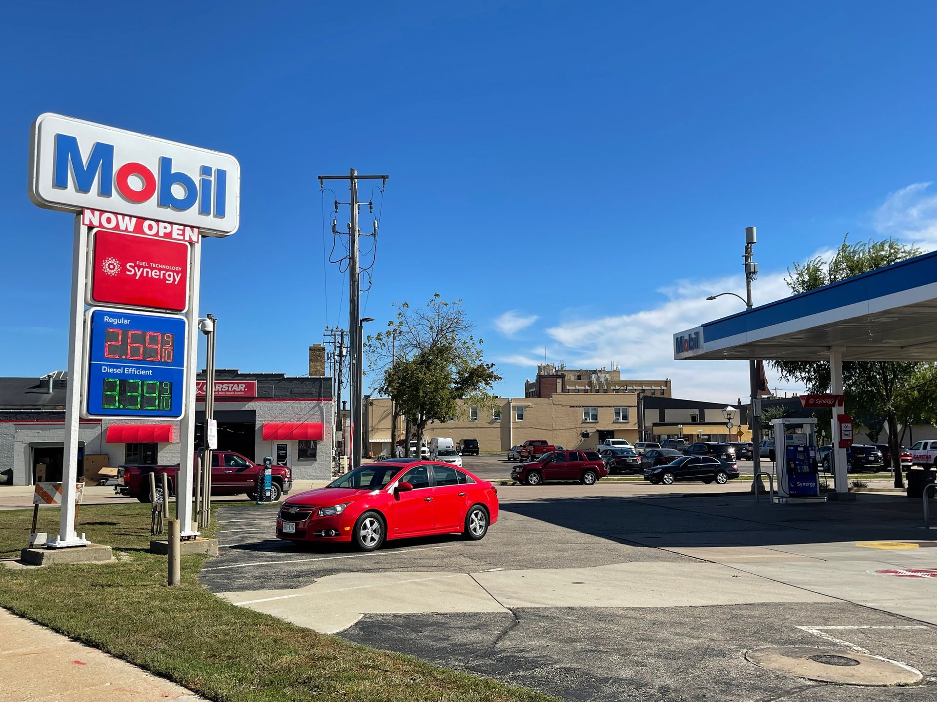Mobil gas station with price sign. Red car drives by pumps on a sunny day.