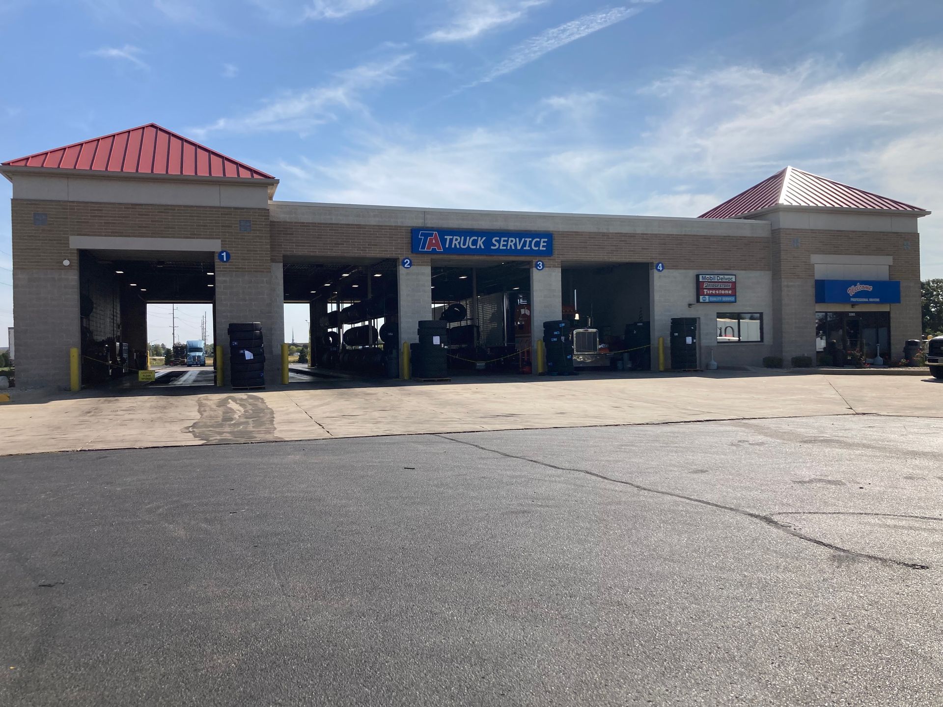 Truck service station with open bays, red roof accents, and blue sky.