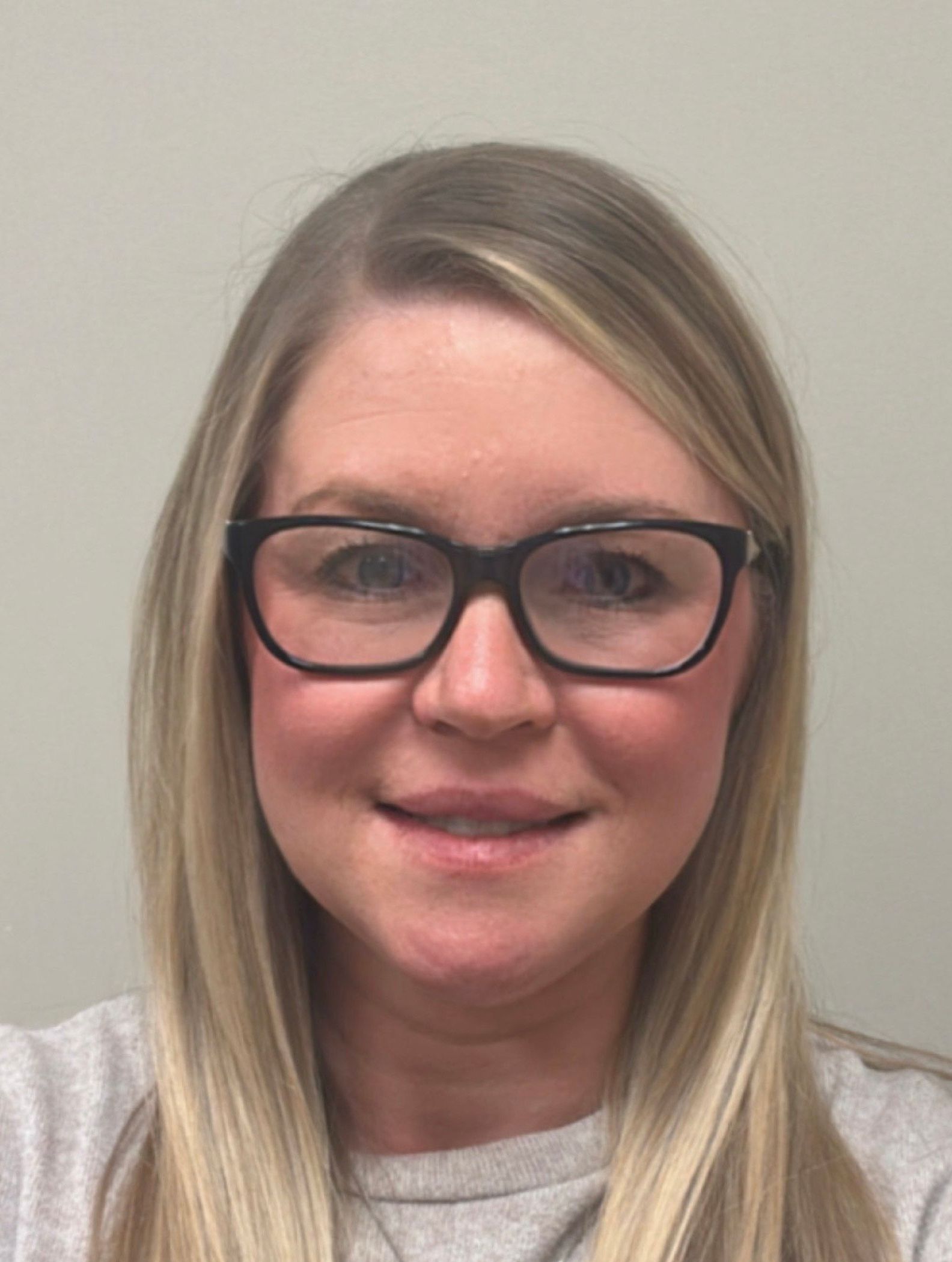 Woman with blonde hair and glasses, smiling, looking at the camera.