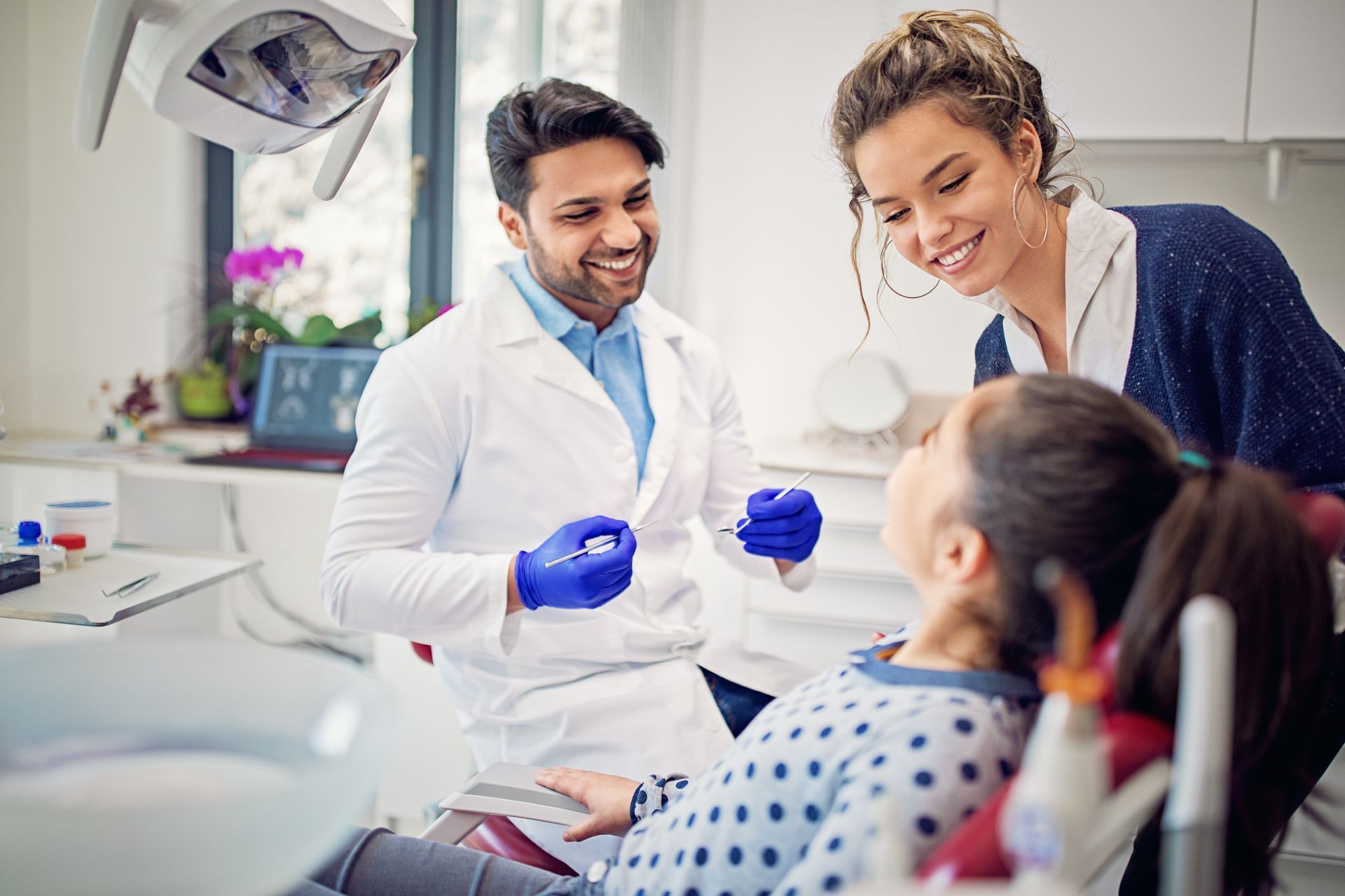 A young girl sits in a dentist chair with a man, showcasing a caring family dentistry experience. 