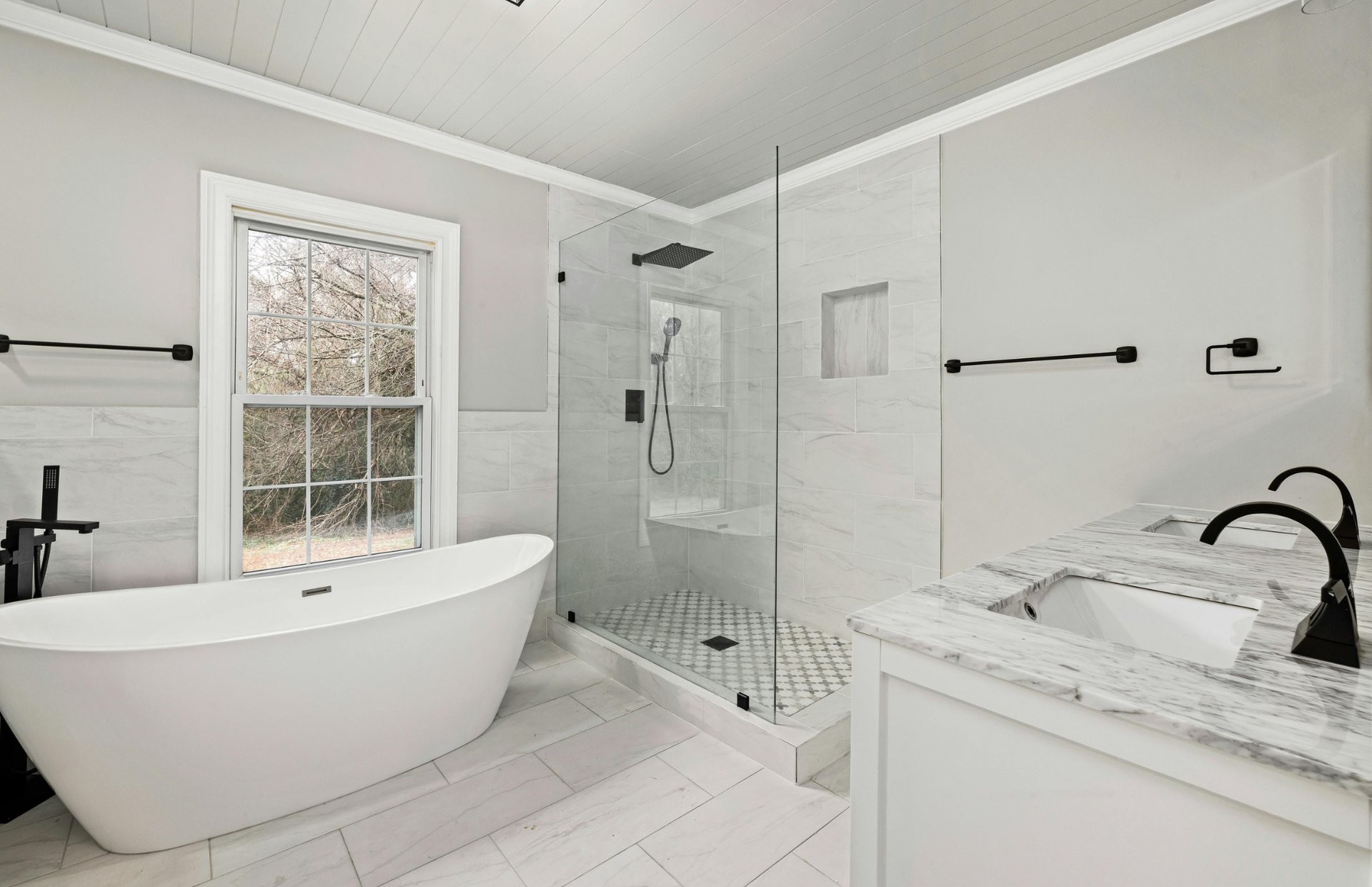 Bright white modern bathroom with freestanding tub, glass shower, vanity, and black fixtures