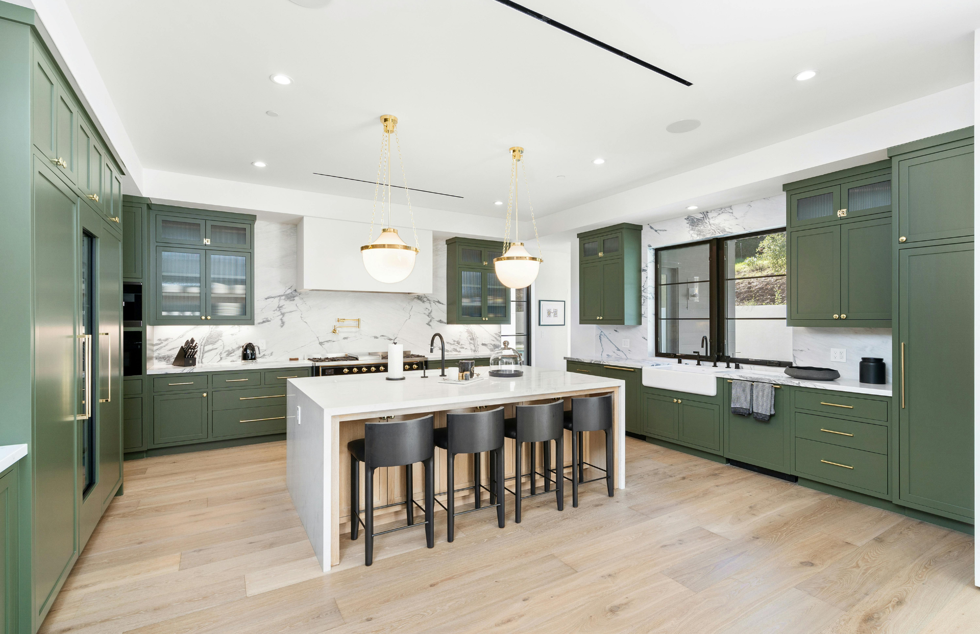 Modern green kitchen with large island, bar stools, pendant lights, and light wood floors