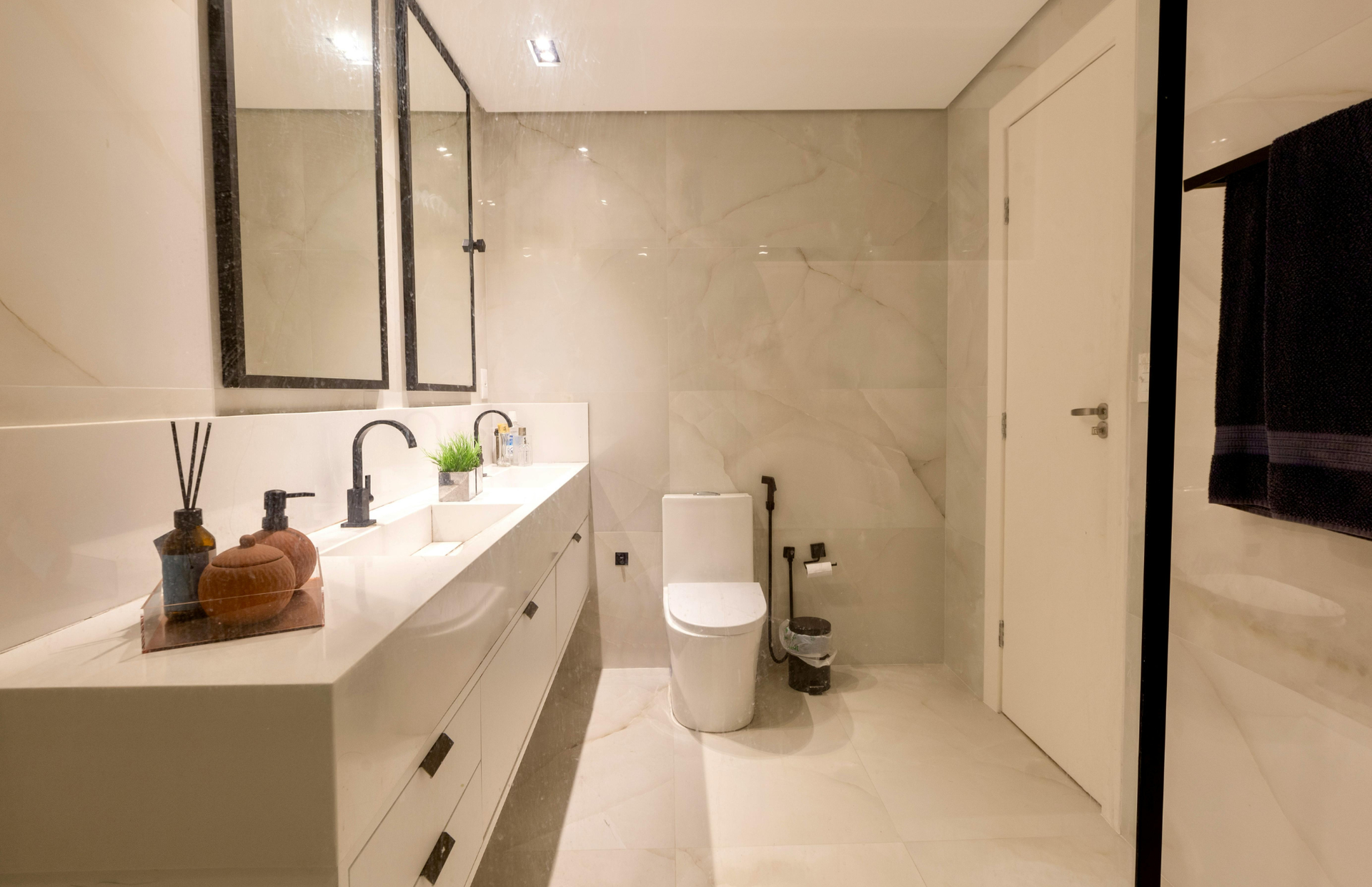 Modern white bathroom with vanity, toilet, glass shower, and beige marble-style walls and floor