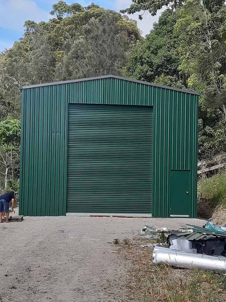 Man Is Standing In Front Of A Green Metal Building — Providing Steel & Concrete Construction In Byron Bay, NSW