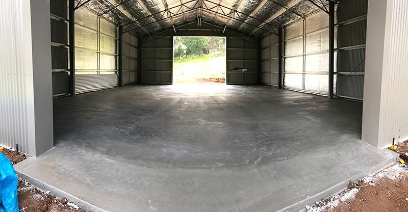 Large empty garage with the door open and a concrete floor — Providing Steel & Concrete Construction In Tweed Heads, NSW