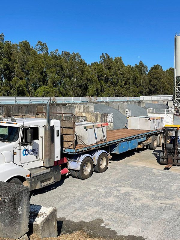 A Semi Truck With A Flatbed Trailer Is Parked In A Parking Lot With Concrete Precast Blocks — CJR Group Concrete Construction In Lismore, NSW