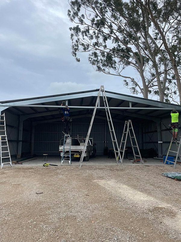 Man Building The Steel Shed Standing On The Ladder — CJR Group Concrete Construction In Byron Bay, NSW