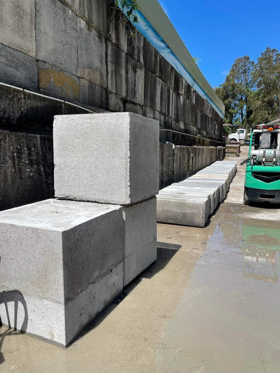 A Green Forklift is Carrying a Stack of Concrete Blocks — Providing Steel & Concrete Construction In Eviron, NSW