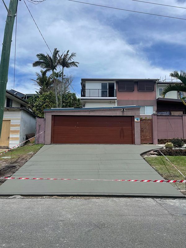 A Concrete Driveway Leading To A Large House With A Wooden Garage Door — CJR Group Concrete Construction In Lismore, NSW