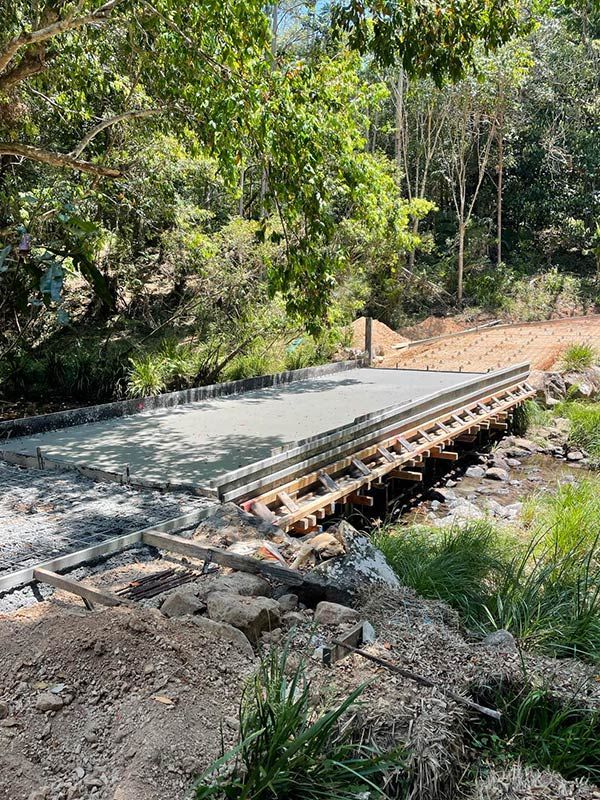 A Bridge Is Being Built Over A River In The Woods — CJR Group Concrete Construction In Gold Coast, QLD