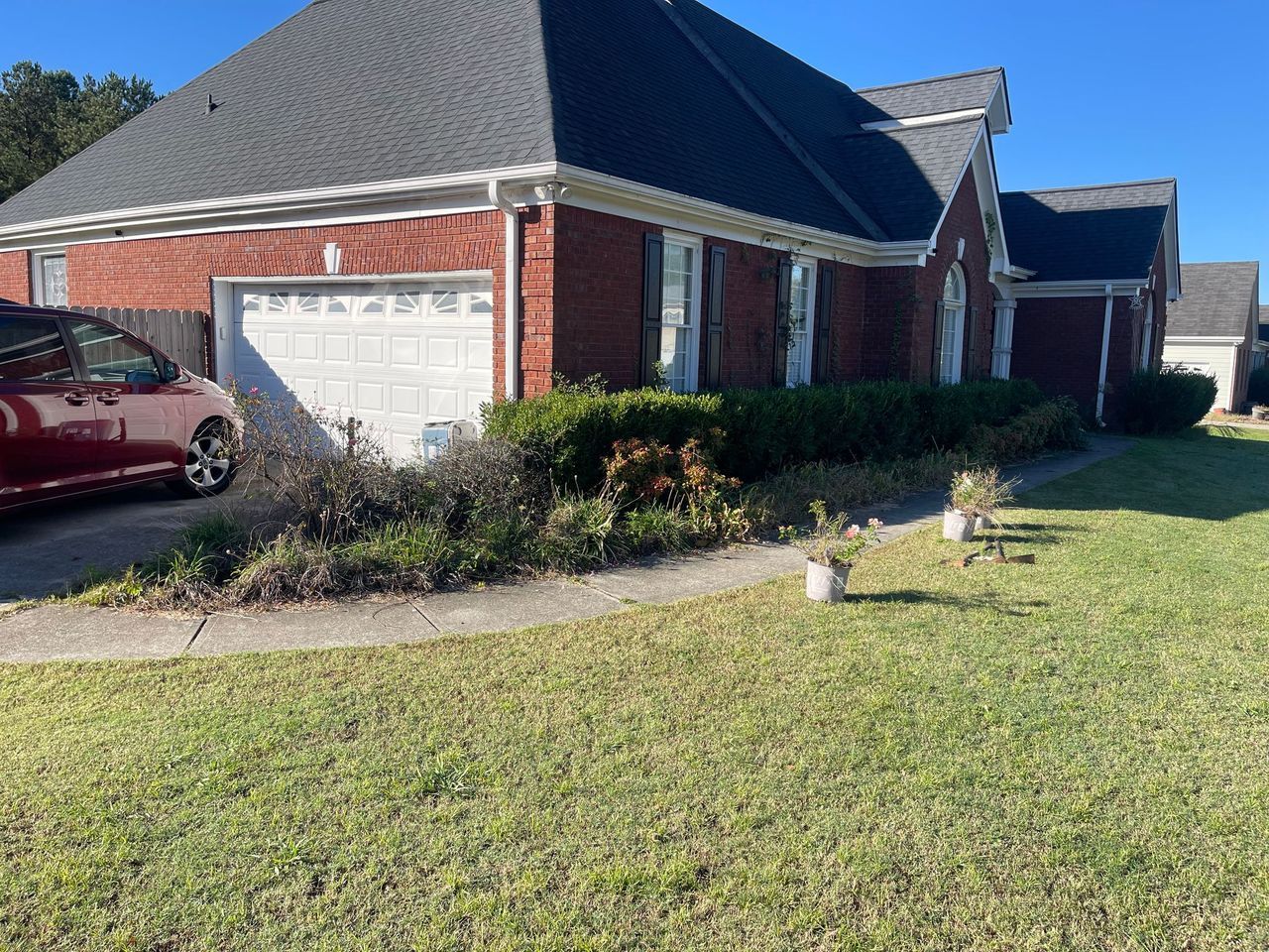 A red brick house with a white garage door, dark roof, and green lawn, under a bright blue sky.