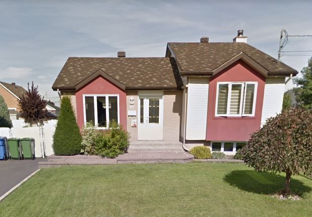 Une maison de banlieue de plain-pied avec un toit brun, un bardage beige et deux parties à pignons rouges avec des fenêtres à cadre blanc.
