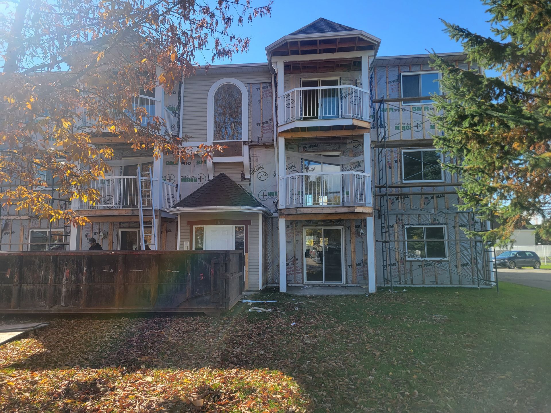 Un immeuble d'appartements en construction, avec isolation extérieure apparente, balcons et benne à ordures au premier plan.
