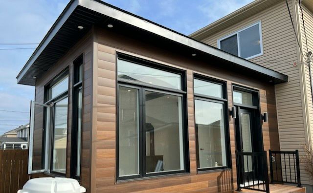 Extension moderne de maison avec bardage horizontal brun, grandes fenêtres à cadre noir et toit plat aux finitions noires.