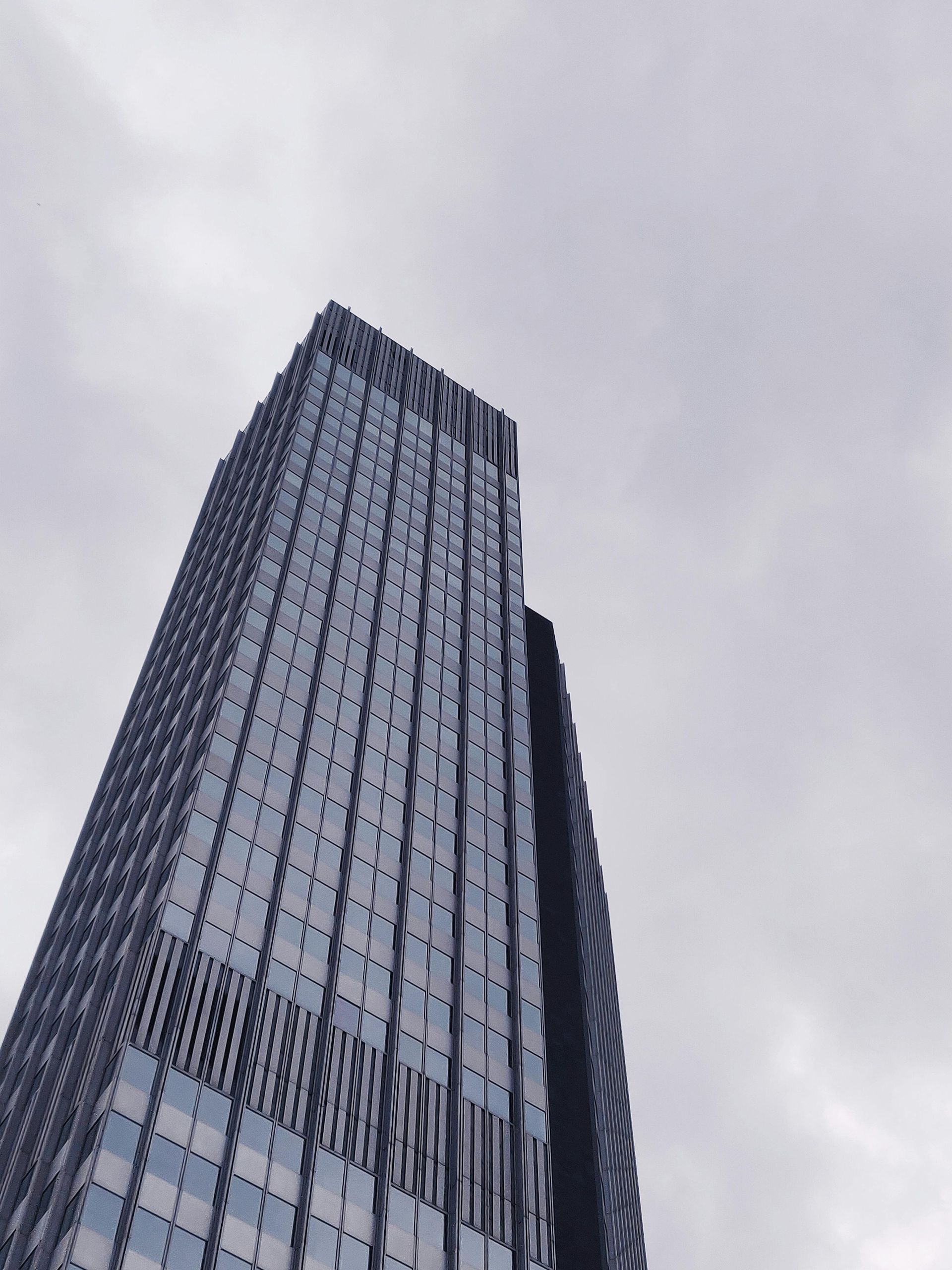 Tall modern skyscraper viewed from below against a cloudy gray sky.