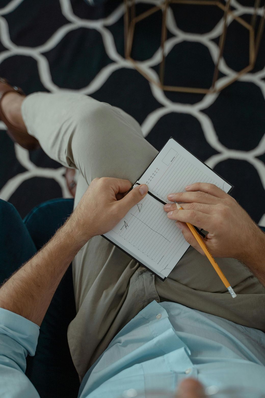 A man is sitting on a couch writing in a notebook with a pencil.