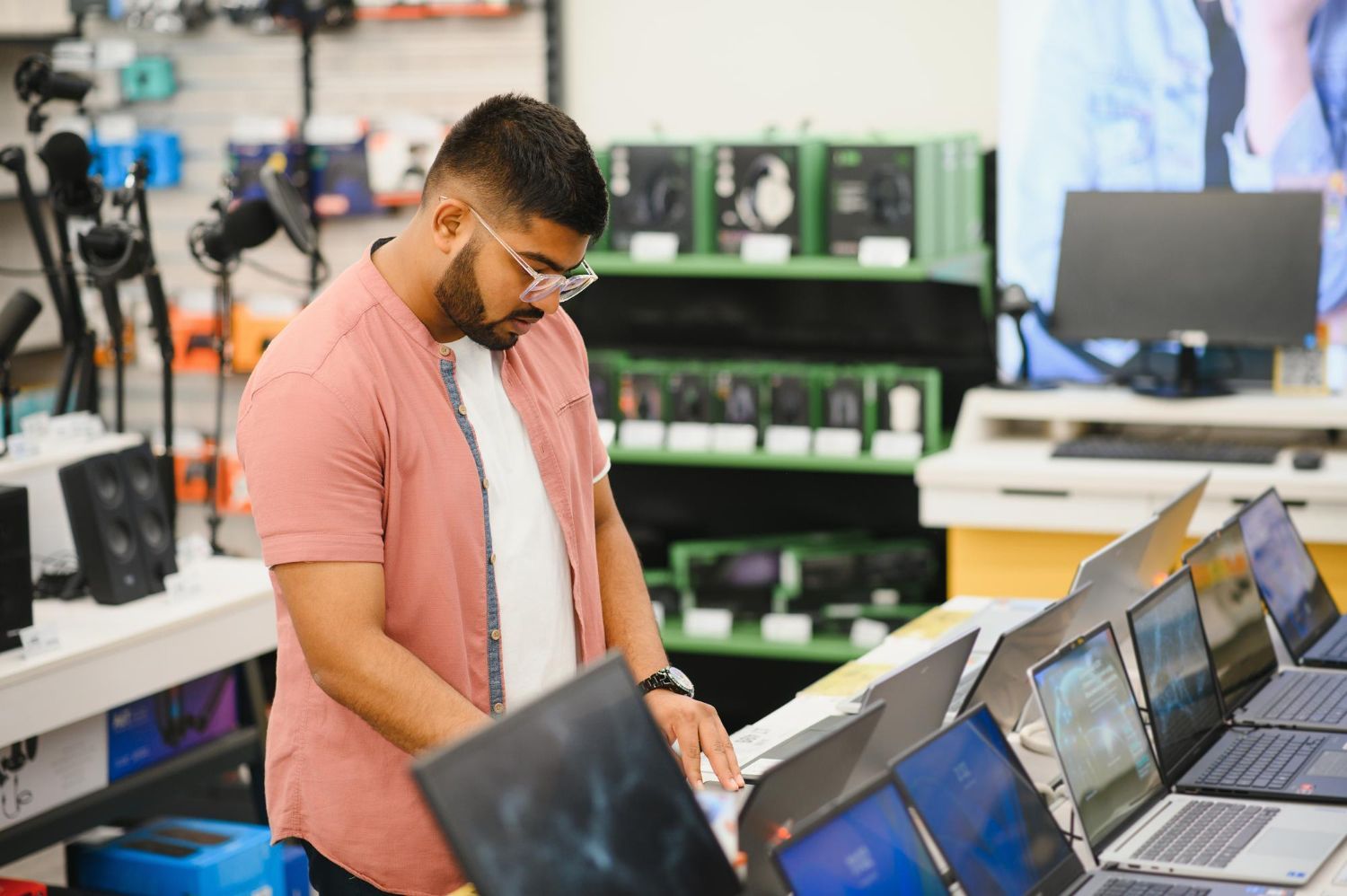 Man examining open laptops in an electronics store aisle
