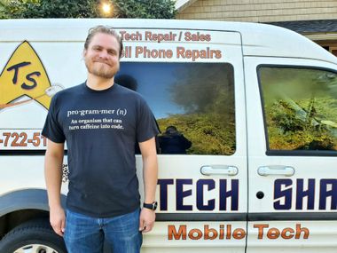 Man standing in front of a white mobile tech repair van with bold blue and orange lettering