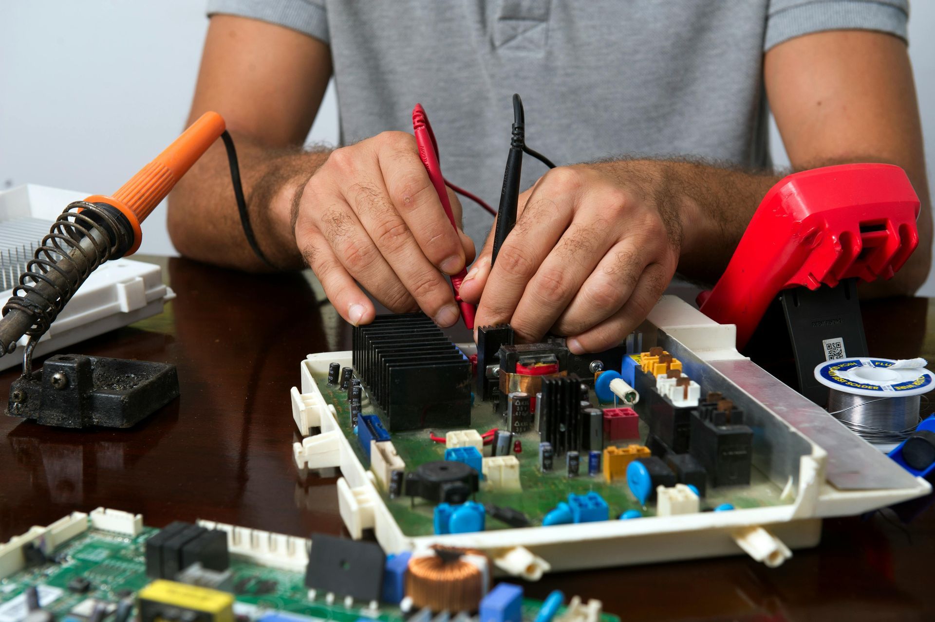 Hands repairing an electronic circuit board with wires and tools on a table