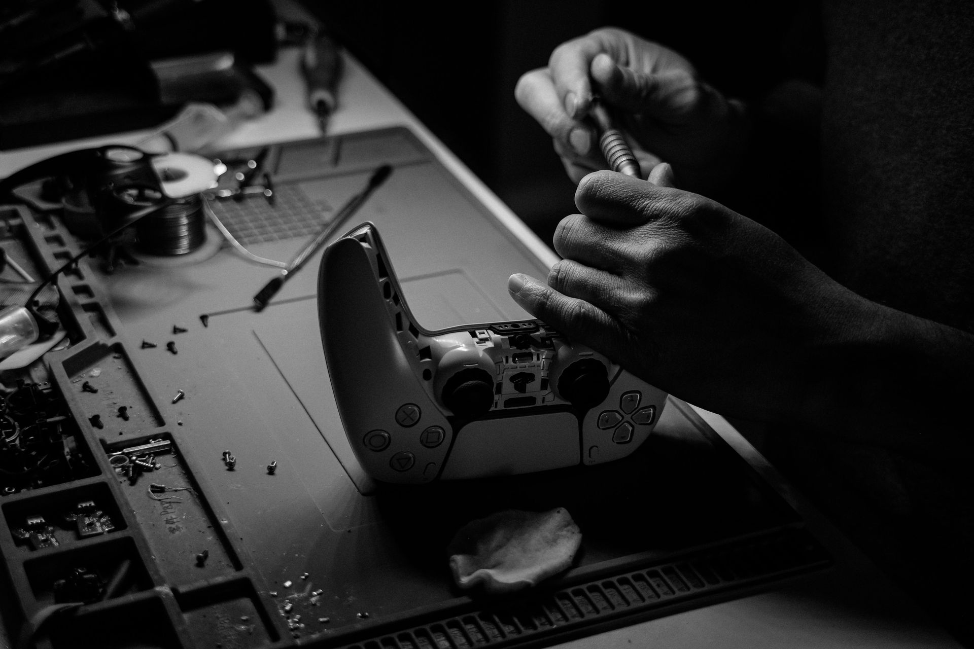 Hands disassembling a game controller on a workbench under focused light