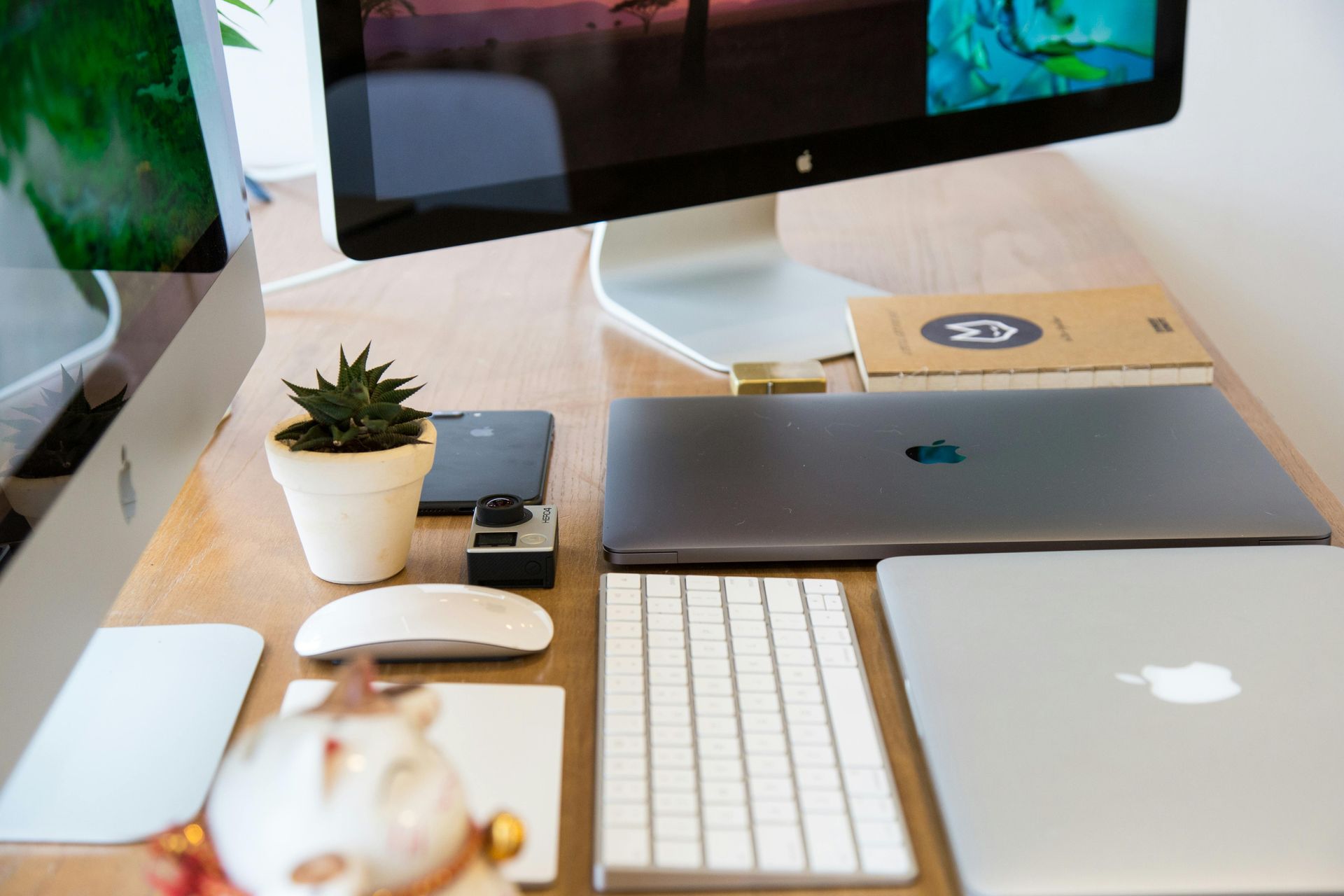 Minimalist desk setup with two Apple monitors, laptop, keyboard, mouse, and small plant