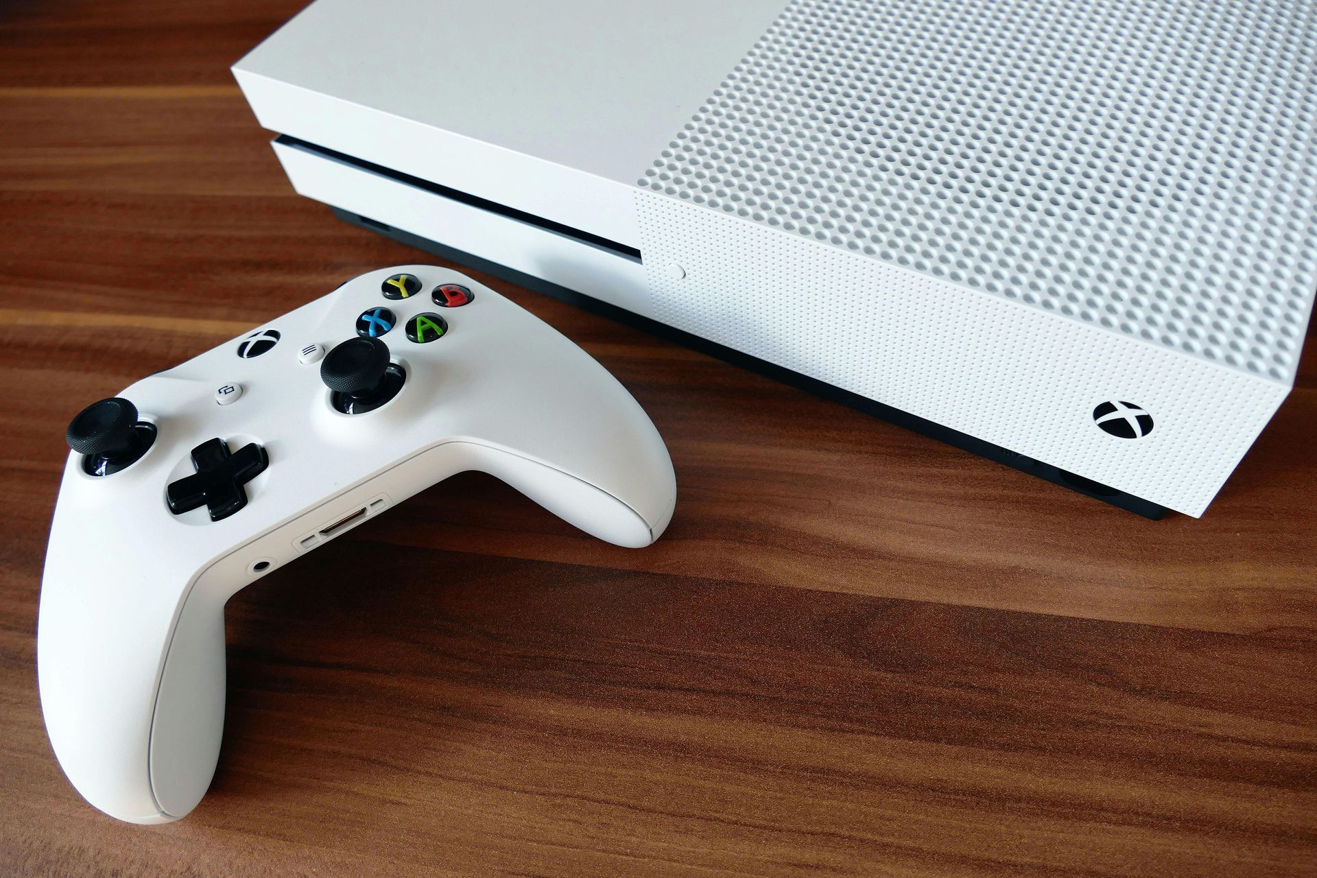 White Xbox console beside a white controller on a wooden surface